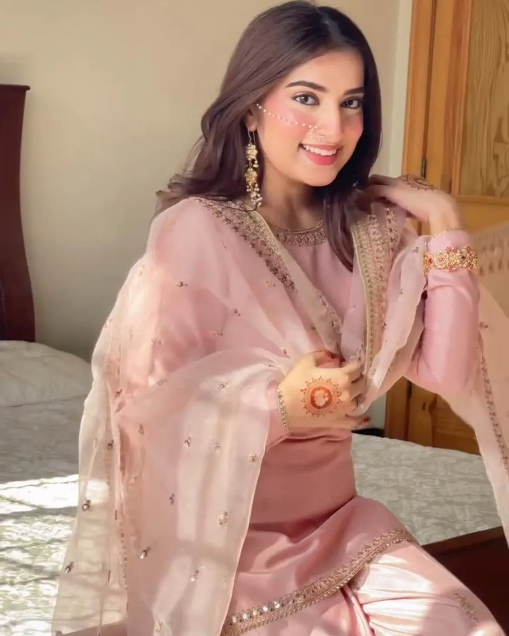 Woman in a pink traditional outfit with gold accents, sitting indoors.