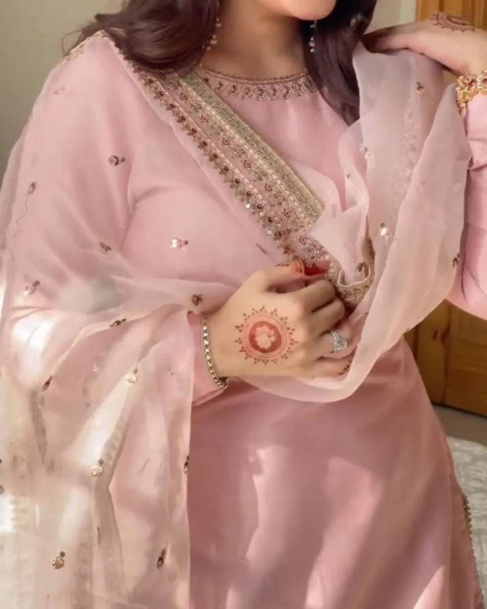 Person wearing a pink traditional outfit with intricate designs, holding a small red object.