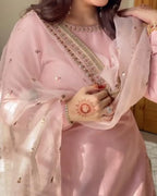 Person wearing a pink traditional outfit with intricate designs, holding a small red object.